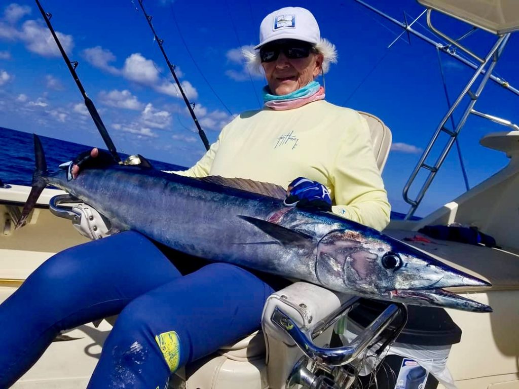 An angler on a fighting chair with a freshly caught Wahoo on a boat with Outcast Charters Cayman, the Cayman Islands