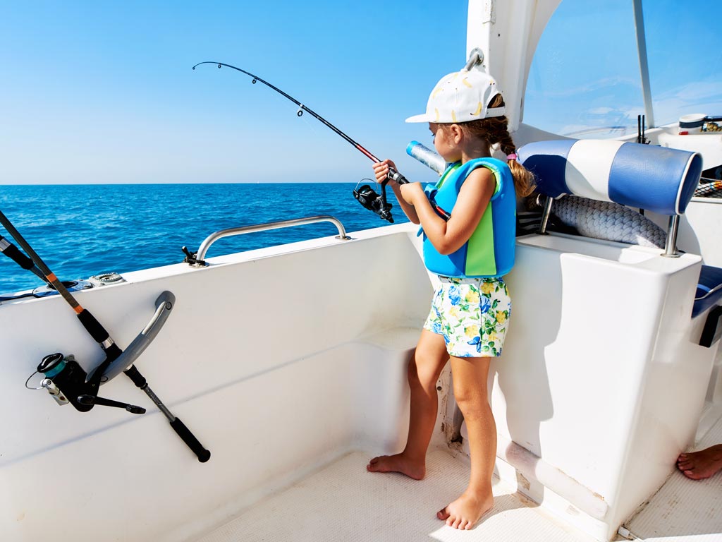 A young girl fishing over the side of the boat.