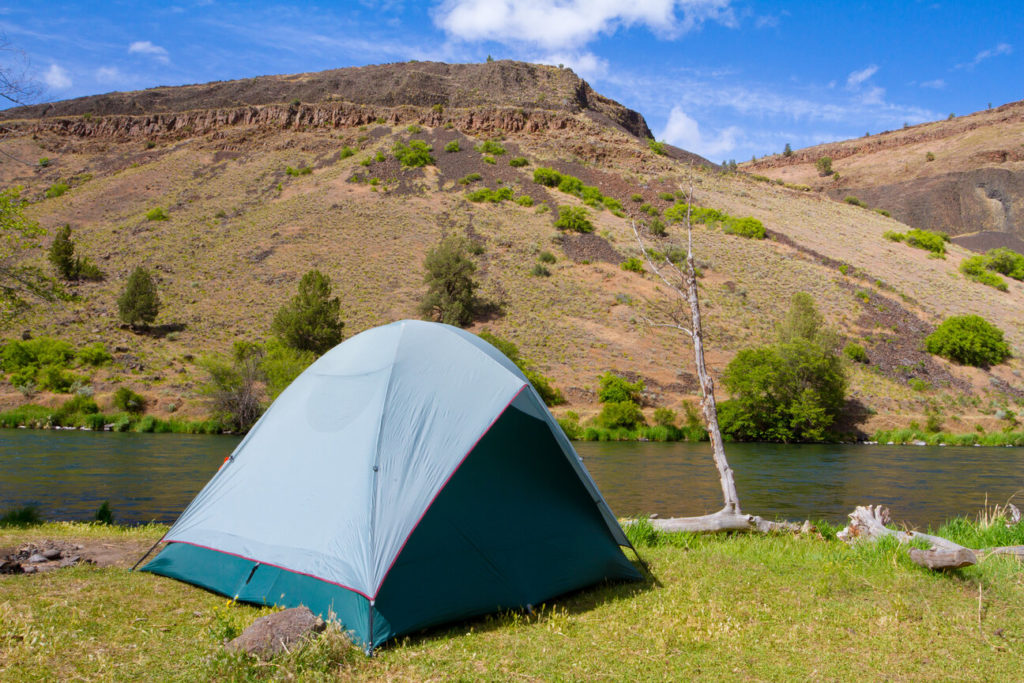A tent campsite on the Deschutes River in Oregon next to a boat and the river.