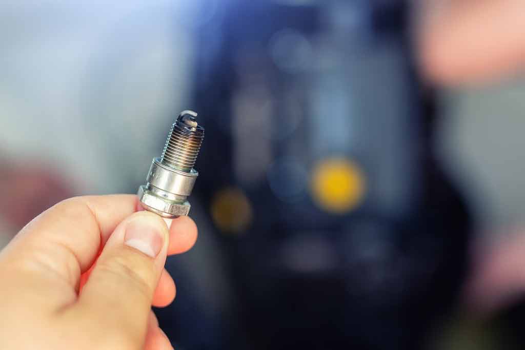 A close-up of a used spark plug in a man's hand
