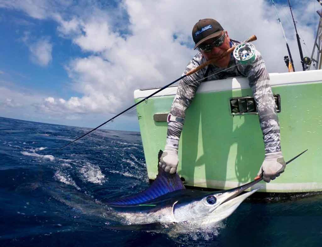 A view of an angler with a fly rod in his mouth and Marlin caught while deep sea fishing in Hawaii