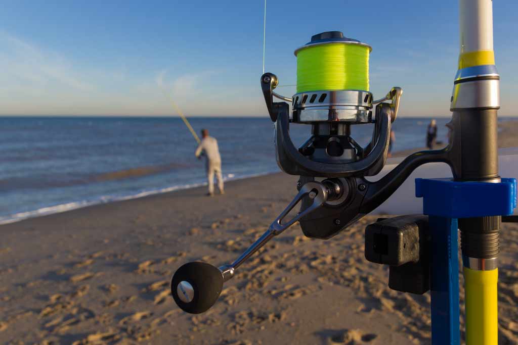 A close-up of a surf fishing rod, with a surf fisherman in the background