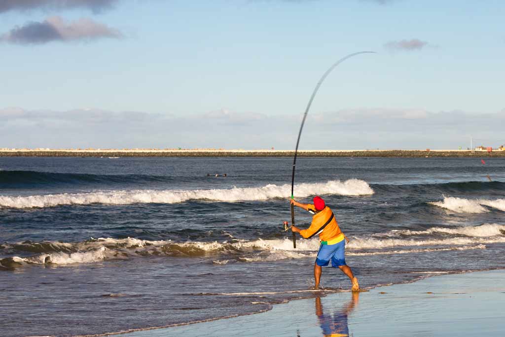 A surf fisherman on a beach, caught mid-cast