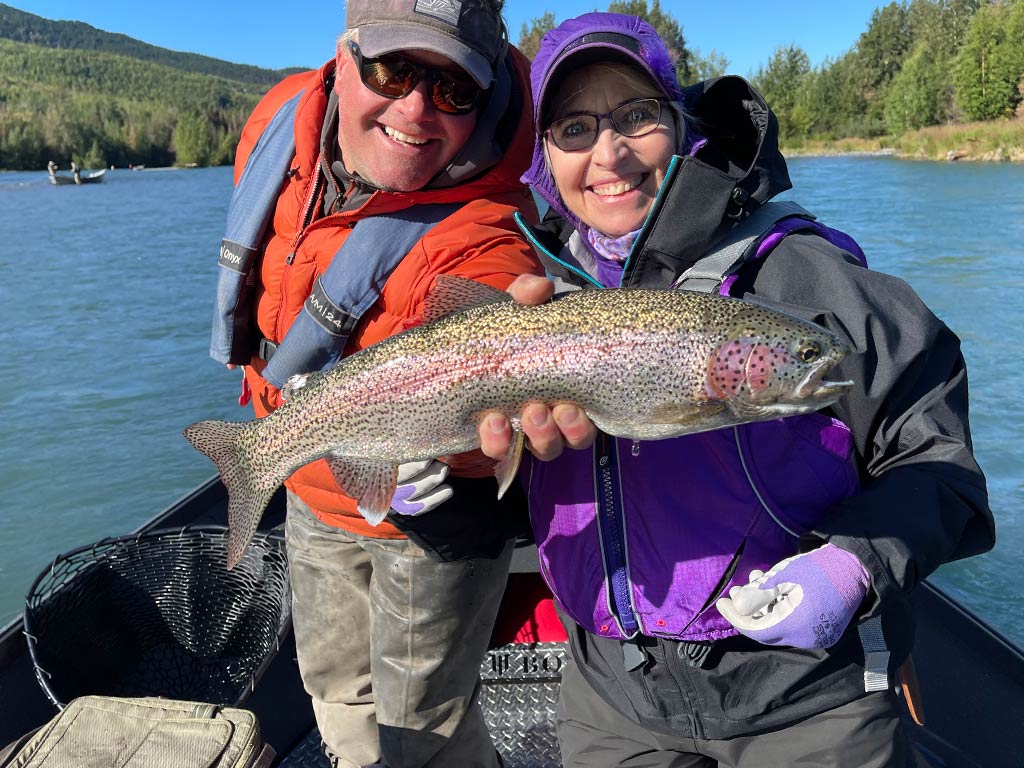 A pair of anglers hold a freshly caught Rainbow Trout on their fly fishing trip in Alaska.