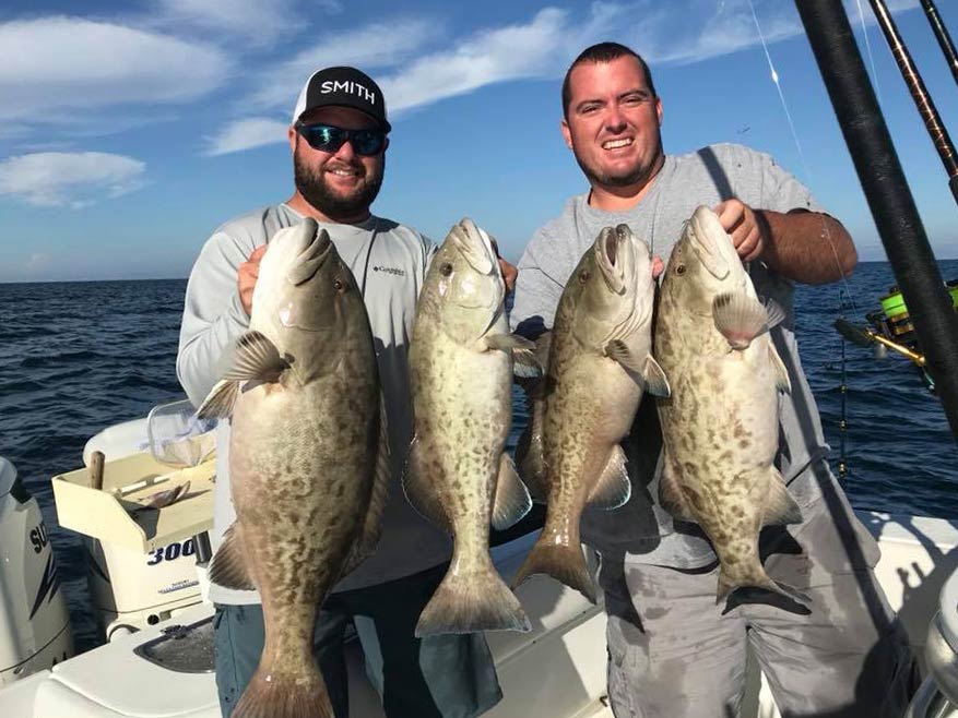 Two smiling anglers on a boat holding two Groupers each, Clearwater, FL