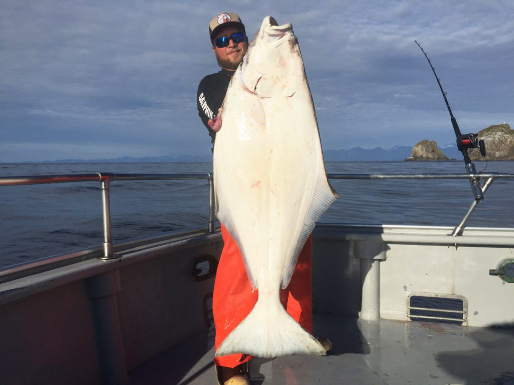 A angler holds up a large Halibut on the back of a fishing boat.
