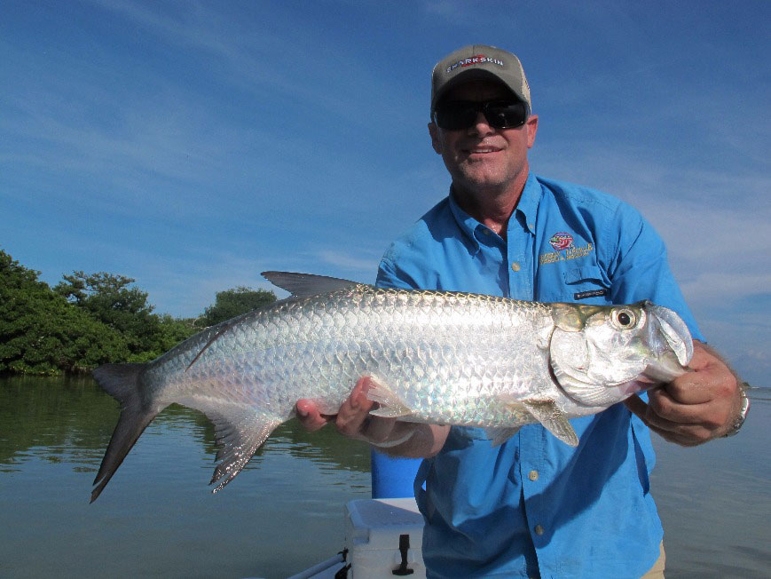 A smiling angler holds a Tarpon caught while flats fishing in the Florida Keys