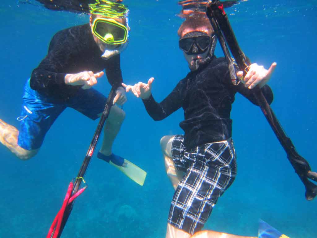 An underwater view of two spearos posing while on their way to go spearfishing in Hawaii