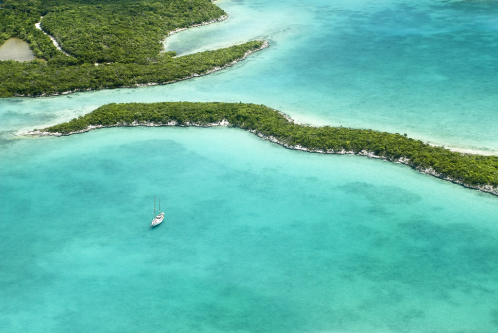An aerial view of an island in the Bahamas with a sailing boat in the water