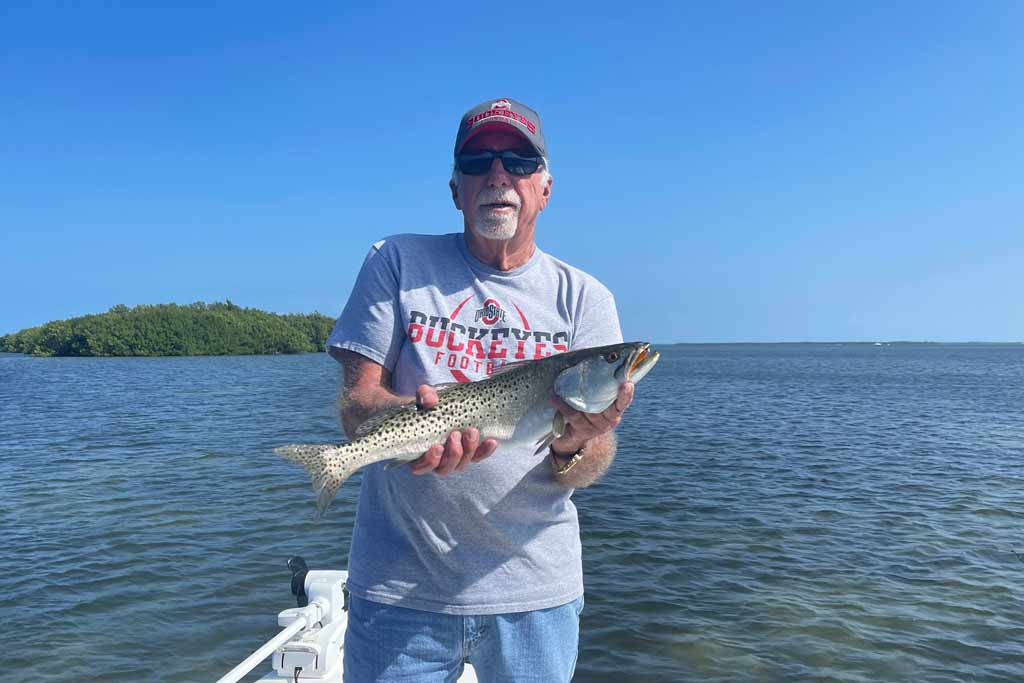 An elderly fisherman holding a Spotted Seatrout while standing on a small boat