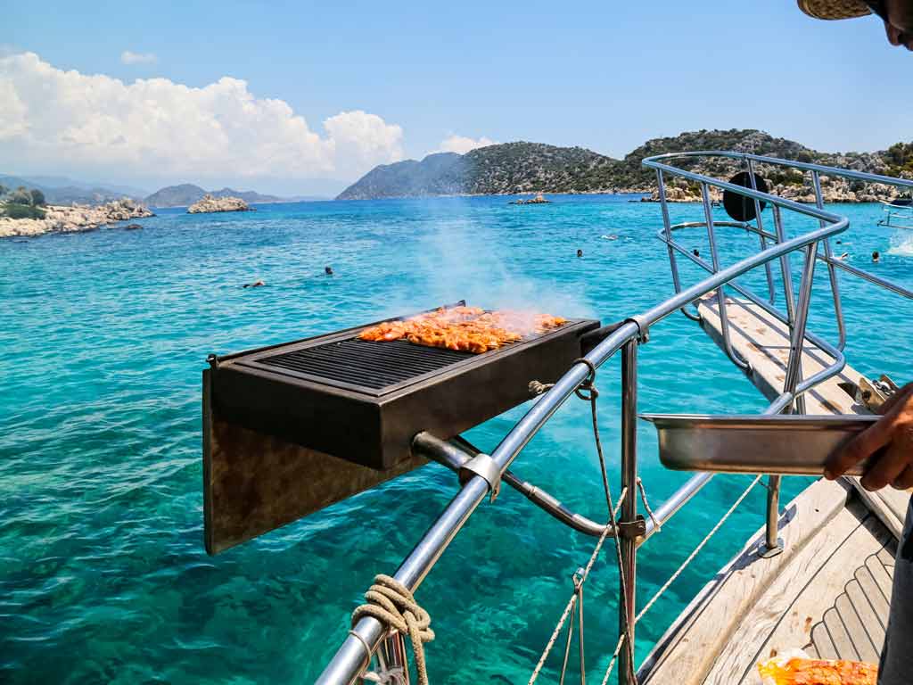 A person cooking food on a boat grill mount while out in the open
