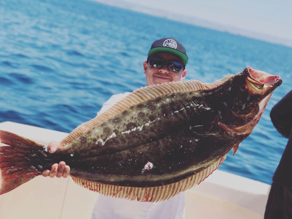 A photo of an angler holding big Halibut with both hands