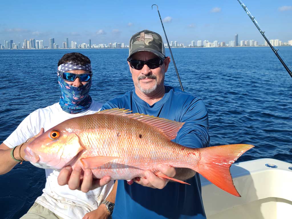 An angler on a boat, holding a Mutton Snapper.