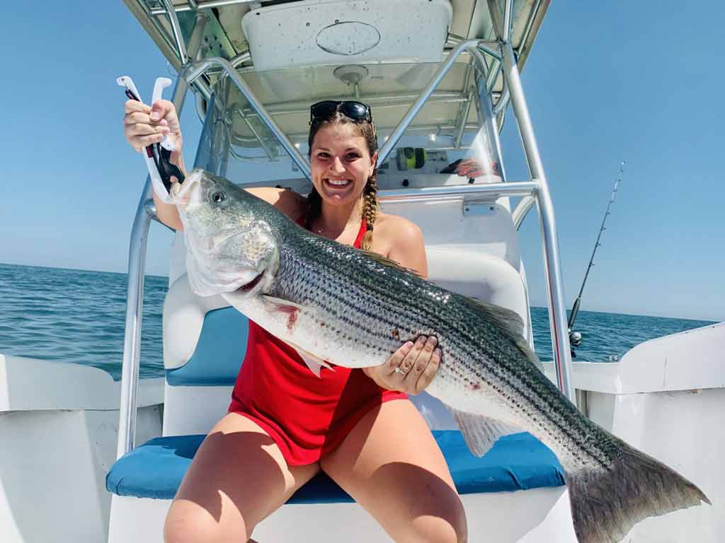 A photo of a girl on a boat holding big Striped Bass caught while fishing in Martha’s Vineyard