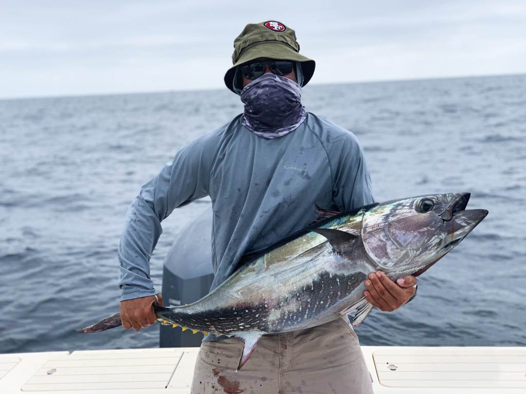 An angler standing on a boat and holding Tuna with both hands