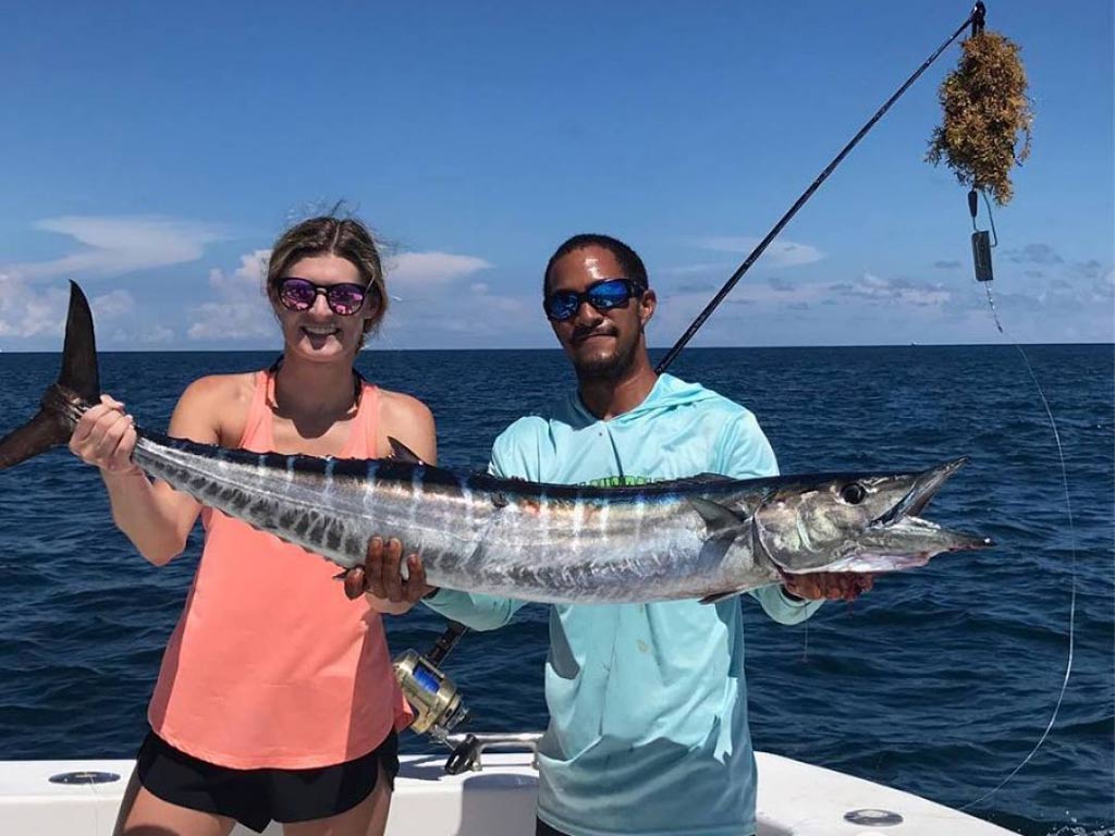 A man and a woman on a boat, holding a big Wahoo they caught.