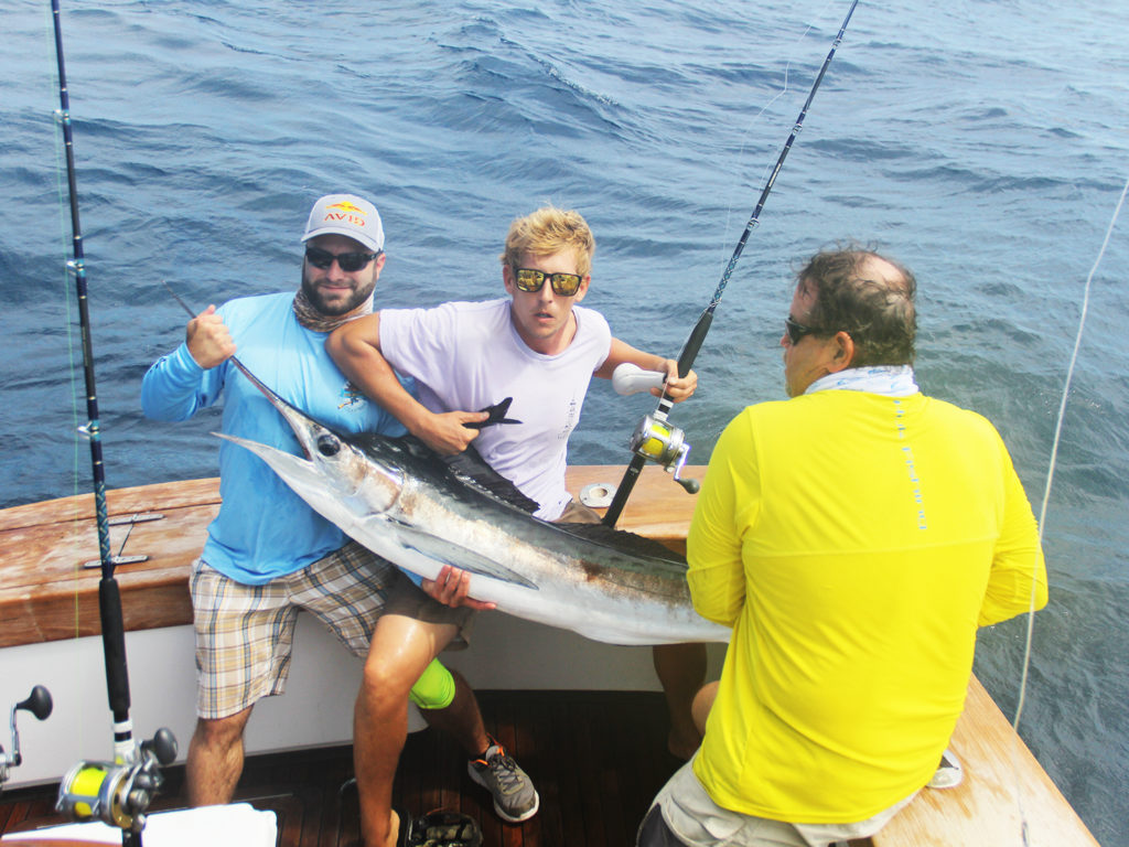 Three anglers holding a freshly caught White Marlin on board an offshore boat in Virginia Beach