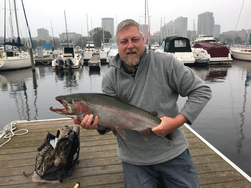 An angler on a pier in Wisconsin after a fishing trip in Lake Michigan with a freshly caught Steehead