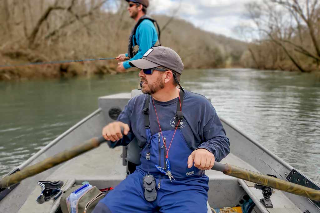 A charter captain rowing his boat and an angler standing behind him