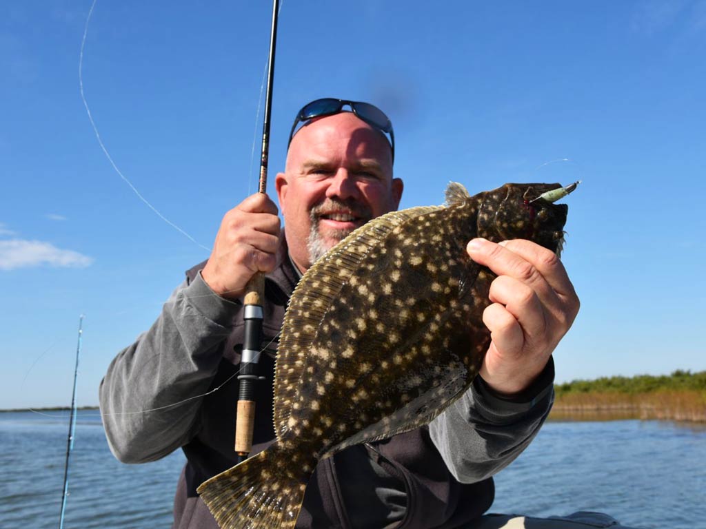 An angler holding Flounder in one hand and a fishing rod in other hand
