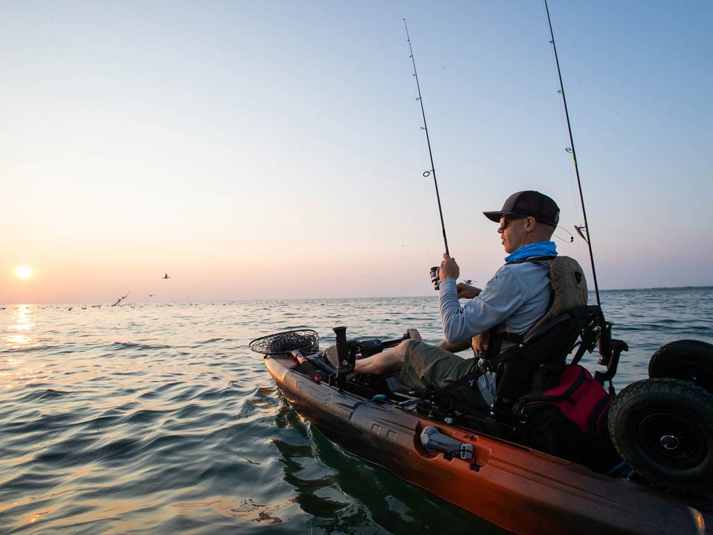 A sunset view of an angler fishing from a kayak on calm waters