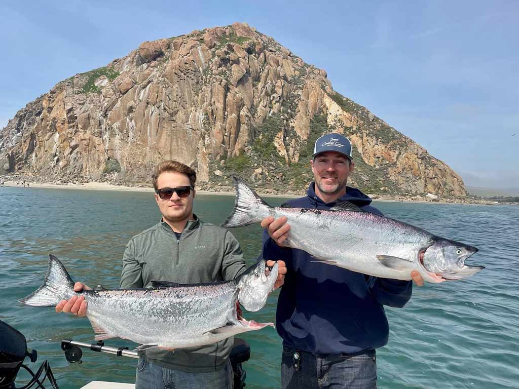 Two anglers posing with Chinook Salmon they caught on their fishing trip, with Morro Rock visible in the background.