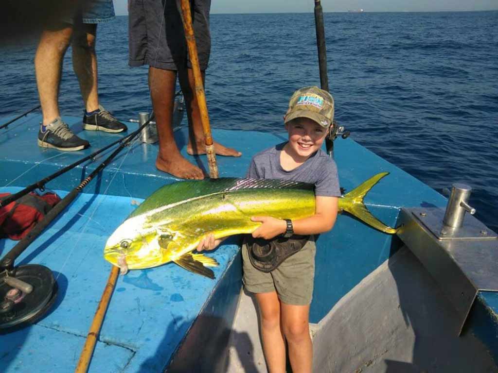 A happy kid holding a Mahi Mahi alone with both hands on a boat