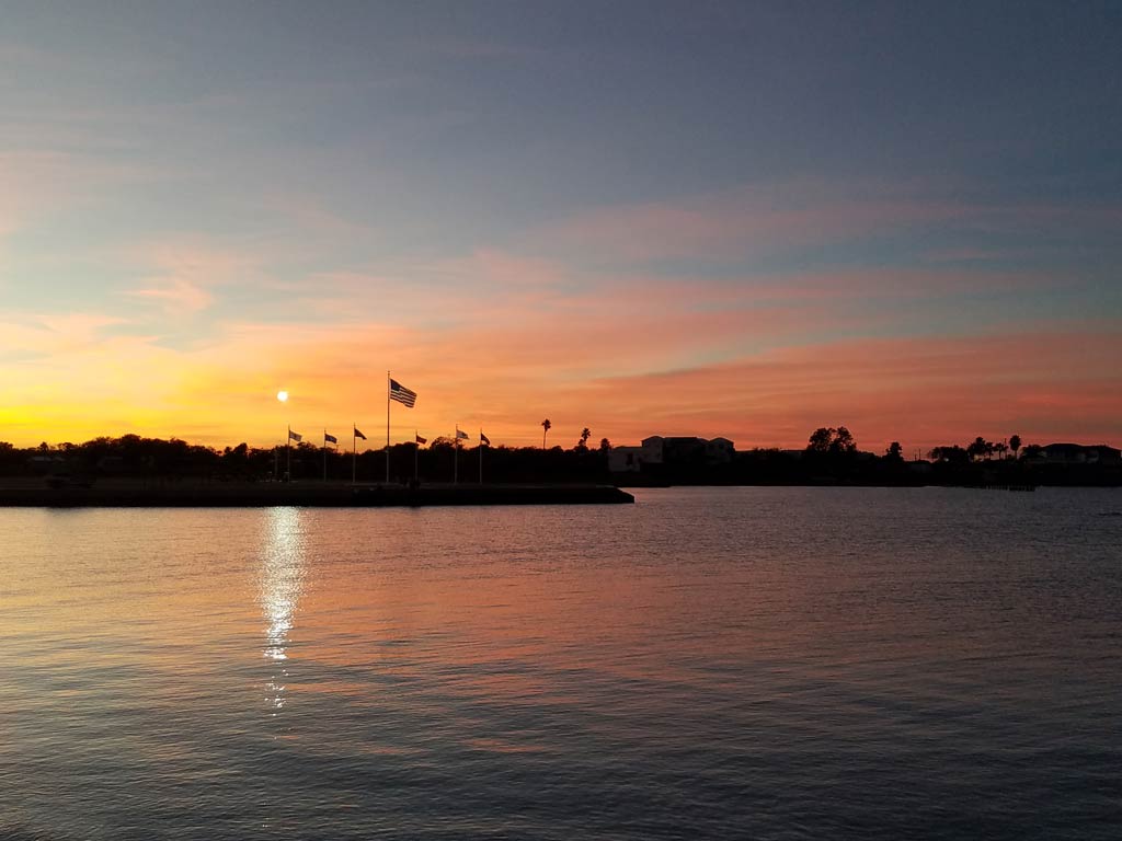 A sunset view of flags, water, and trees in Port Lavaca