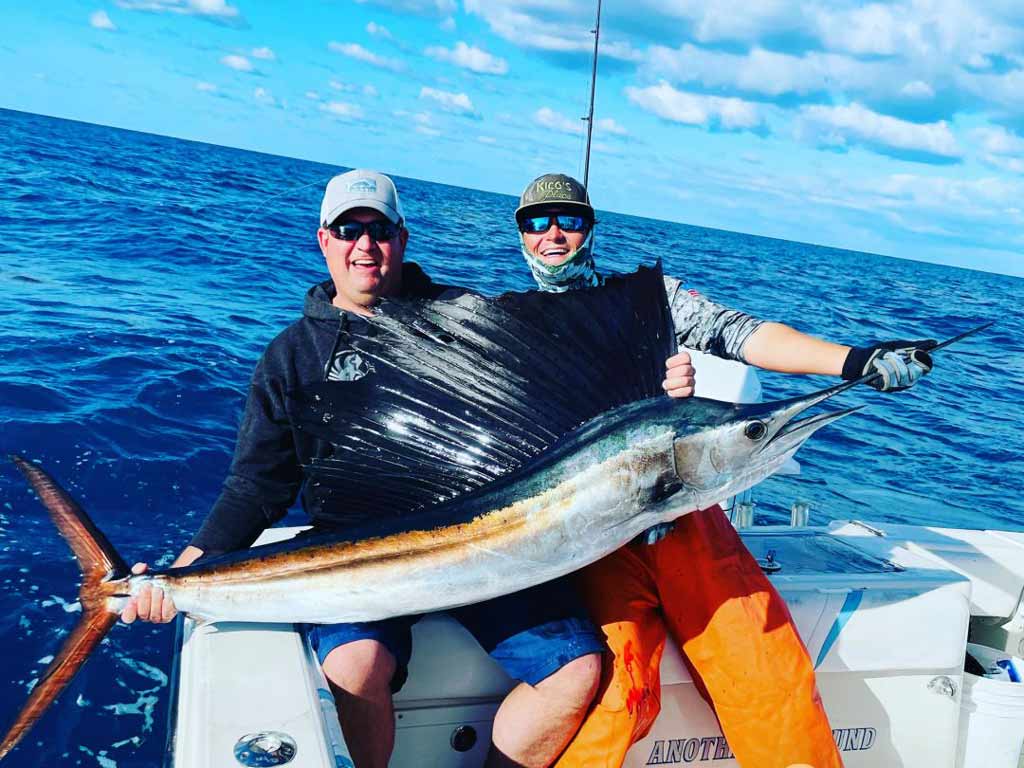 Two anglers sitting on a boat and holding a big Sailfish caught in Islamorada