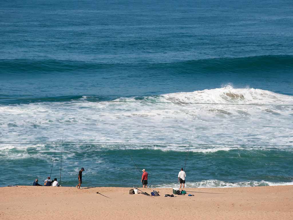 A beach view of anglers fishing from the shore while the seas are choppy and wavy