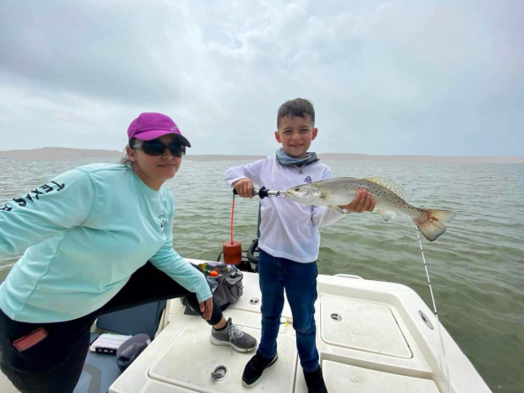 A kid standing on a boat and proudly holding Speckled Trout