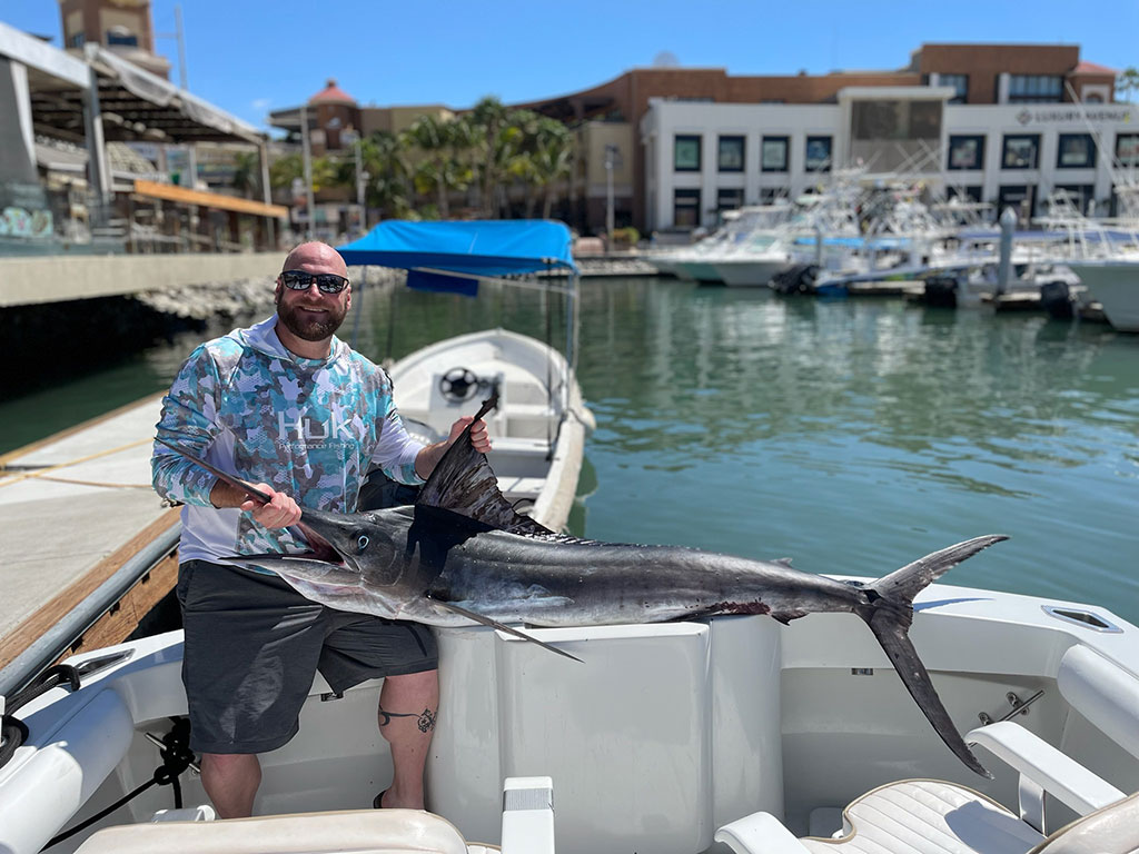 A smiling angler holds a large Striped Marlin back at the dock in Cabo San Lucas