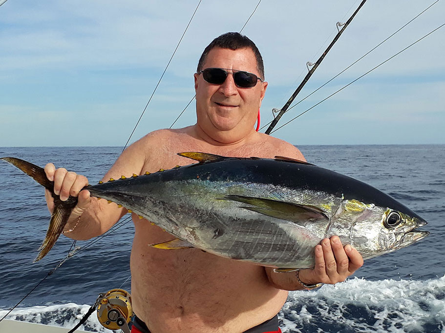 An angler in sunglasses holds a Yellowfin Tuna on the water