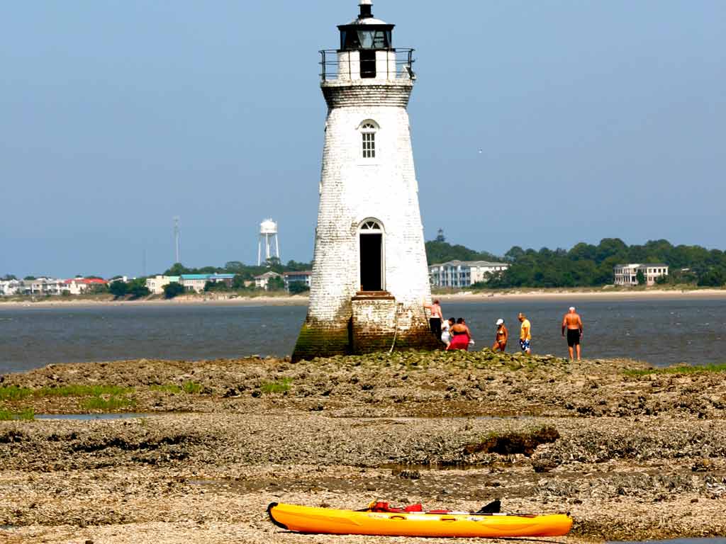 A photo of a yellow kayak ashore with the Fort Pulaski lighthouse visible in the background.