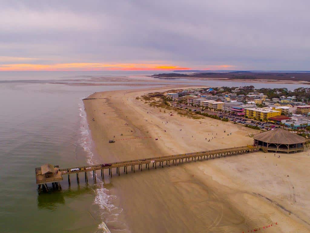 An aerial photo of Tybee Beach pier leading out into the ocean across the sand.