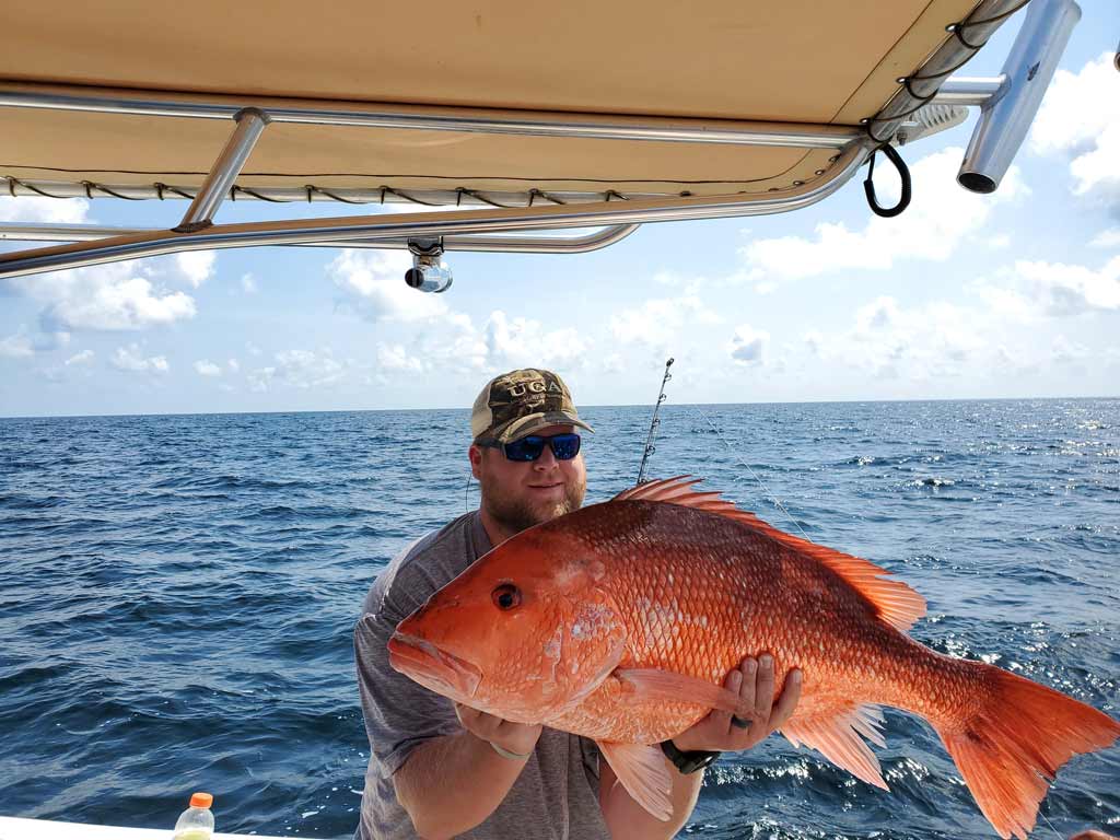 An angler on a boat, holding a massive Red Snapper.