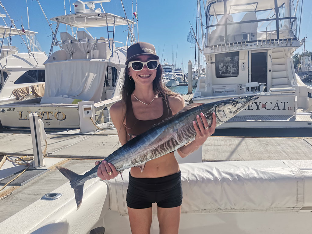 A female angler holds a large Wahoo back at the dock after a successful fishing trip in Cabo San Lucas