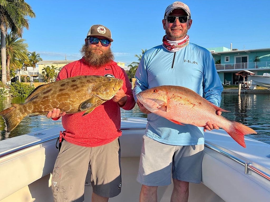 Two anglers hold a Snapper and Grouper after returning to the dock from a successful fishing trip in Key Largo