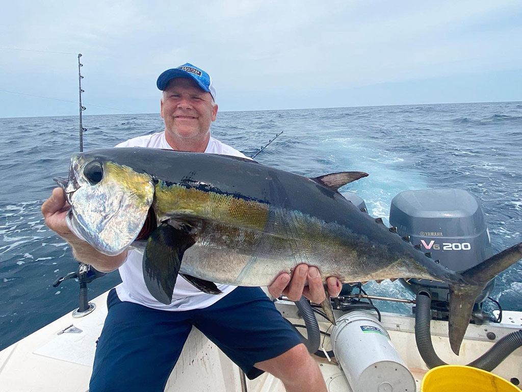 A smiling angler sits on the side of a boat holding a Blackfin Tuna he recently caught.