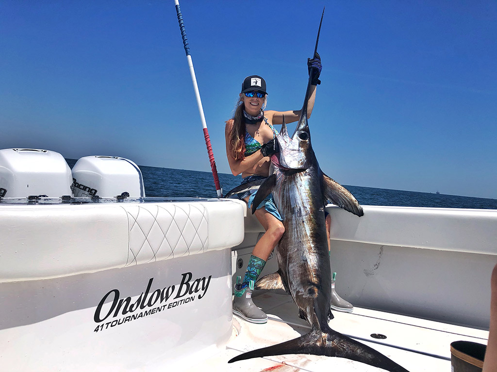 A female angler sitting on the side of a boat and holding a Swordfish which she caught on a Gulf of Mexico fishing trip out of Venice, LA.
