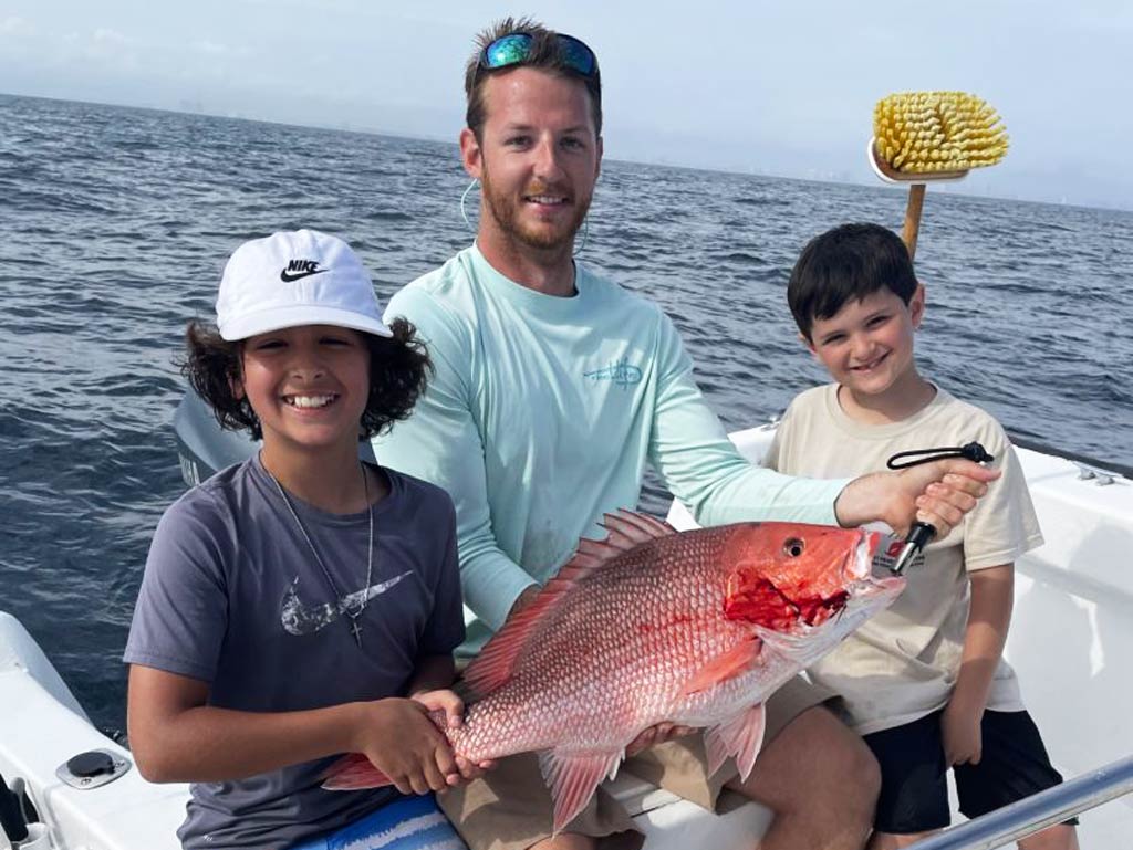 A photo of two kids on the boat with Captain Payton Anderson holding Snapper