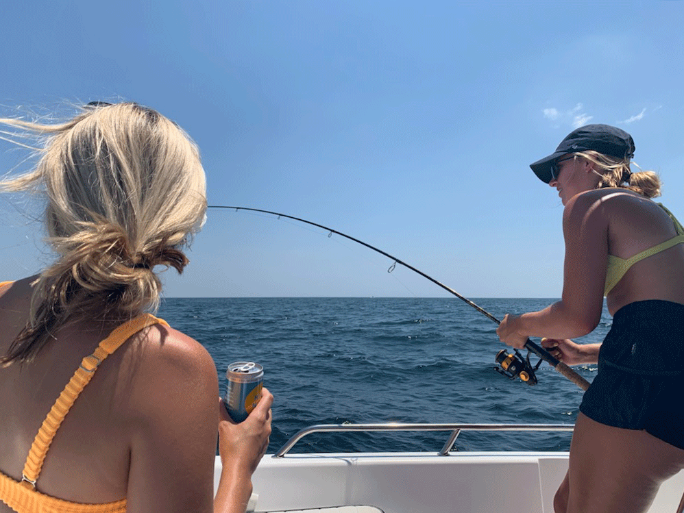 Two young female anglers, one fishing and the other holding a can of soft drink, on a boat in Orange Beach, Alabama.