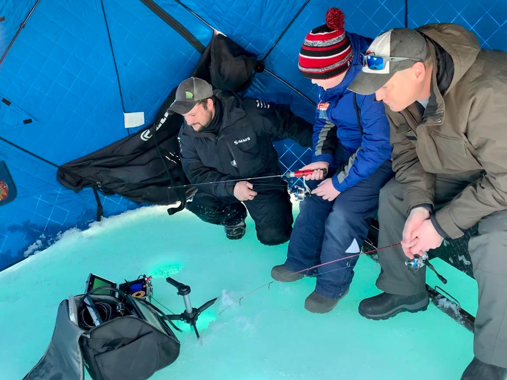 Three anglers ice fishing inside a shanty.