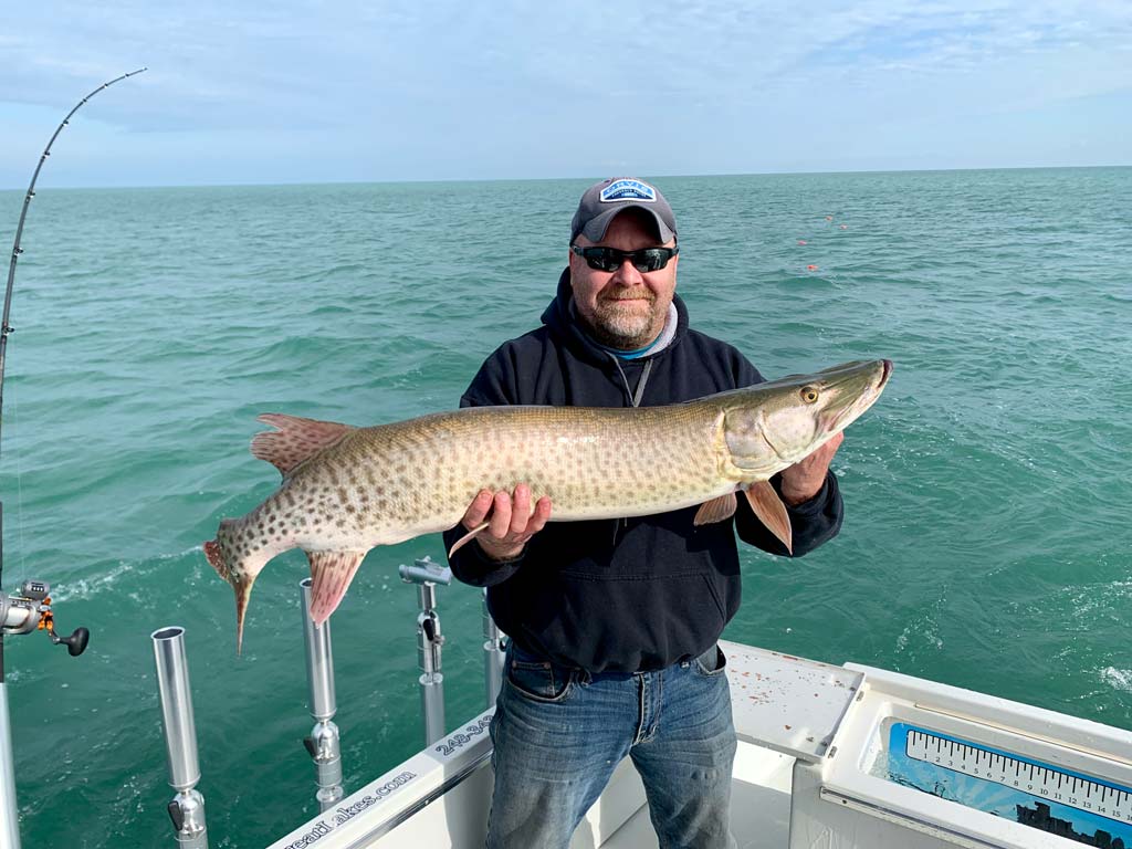 A man on a boat, posing with a Musky he caught fishing on Lake St. Clair in Michigan.