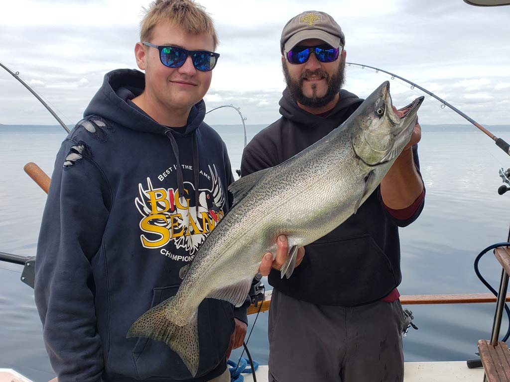 Two men aboard a Lake Superior fishing charter, posing with a King Salmon they caught.