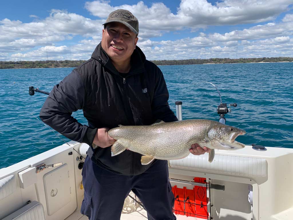 A man on a boat holding a Lake Trout.