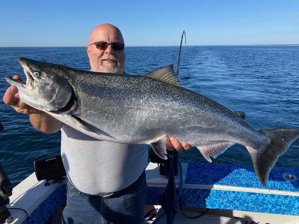 An angler posing with a big Chinook Salmon he reeled in during the peak fishing season on Lake Michigan.