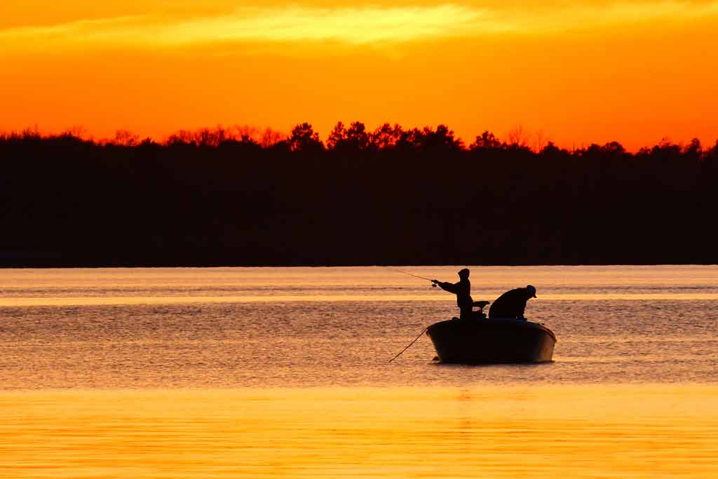 Two fishermen fishing from a boat in the middle of a lake during sunset