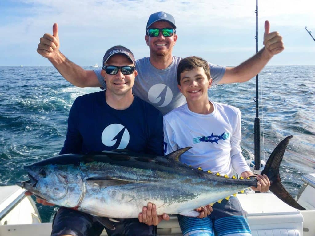 Three male anglers all smiling on a fishing boat in Cape May, NJ, two of them holding a freshly caught Tuna.