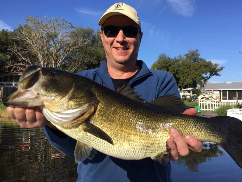 An angler holding a big Largemouth Bass on a boat in the fall